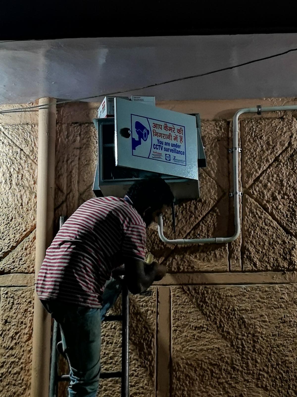 Technician working on cable termination below an installed CCTV equipment enclosure