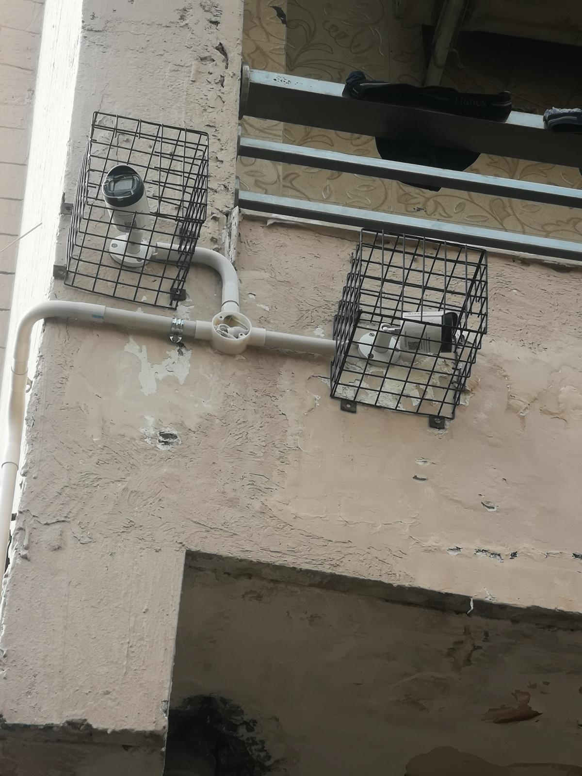 Two caged CCTV cameras mounted on a wall with linked conduit routing