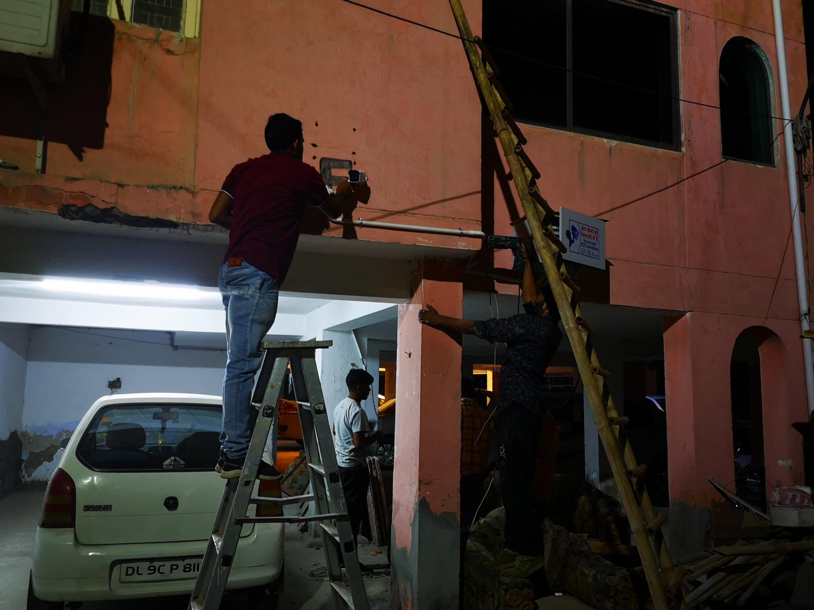 Two technicians mounting cameras and an equipment enclosure on a building at night