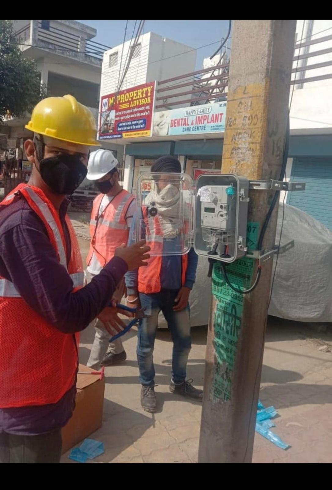 Technicians fitting a protective cover on a pole-mounted electricity meter enclosure